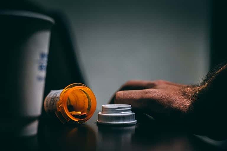 Moodily lit scene of an open prescription bottle and hand on a table, depicting healthcare themes.
